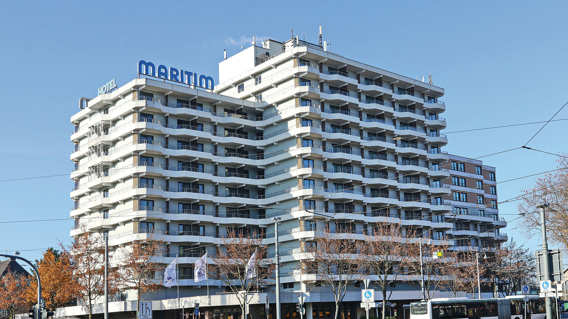 Tagesansicht des Maritim Hotel Darmstadt mit Straßenbahnschienen und vorbeifahrendem Bus im Vordergrund.