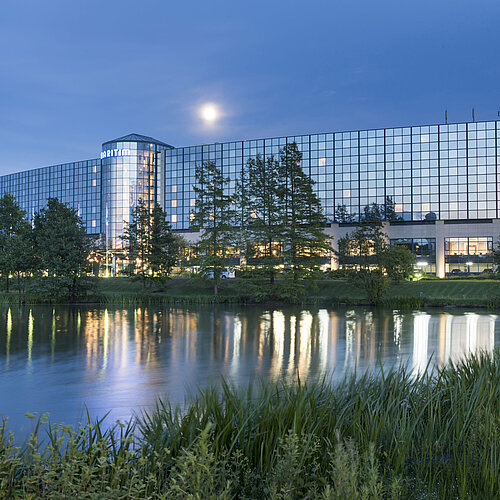 Beleuchtetes Maritim Hotel Hannover mit Glasfassade und Seespiegelung in der Abenddämmerung.